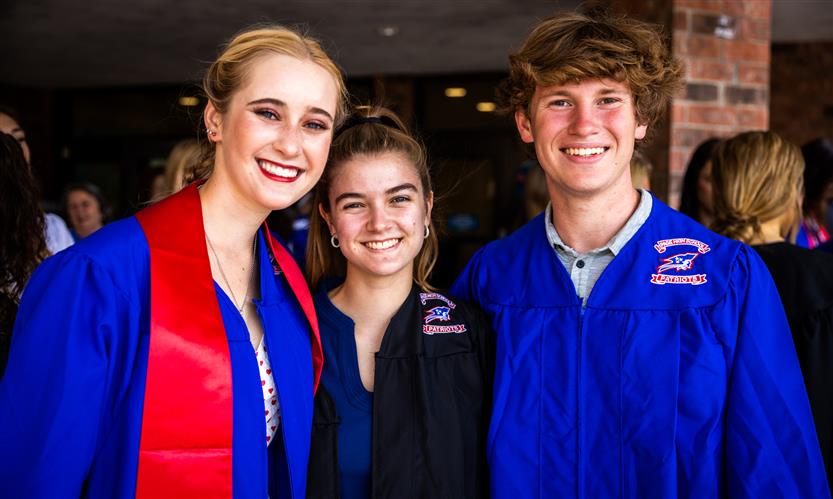 Three seniors in graduation robes smile